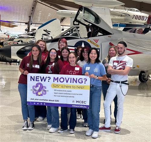 Military kids holding up a banner in the NAS museum advertising moving help for military family.